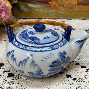 Peut inclure: Une théière en porcelaine bleue et blanche avec une poignée en bambou. La théière présente un motif chinois traditionnel avec des motifs floraux bleus et blancs.