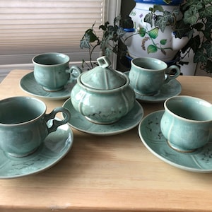 May include: A set of four teal green teacups and saucers with a floral design, and a matching teapot with a lid.