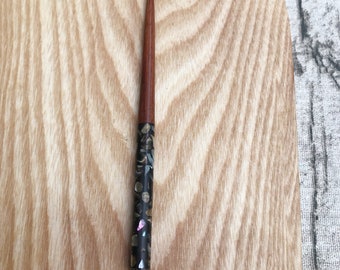 Puede incluir: Un palo de pelo de madera con una sección de patrón negro y blanco. El patrón está hecho de pequeños trozos de material iridiscente.