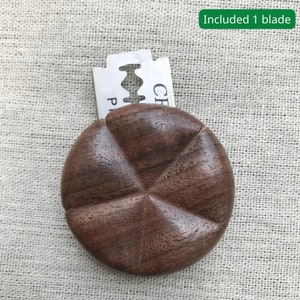 Könnte beinhalten: Ein Rasiererhalter aus Holz mit einer Klinge im Lieferumfang. Der Halter ist aus dunkelbraunem Holz und hat eine runde Form mit einem fünfzackigen Sternmuster.