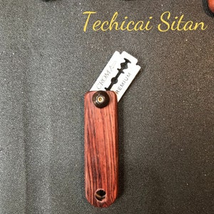 Puede incluir: Un mango de navaja de afeitar de madera con una cuchilla de afeitar plateada unida. La cuchilla está etiquetada como "Croma Premium".