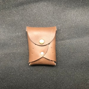 Könnte beinhalten: Eine braune Ledergeldbörse mit zwei Druckknöpfen und einer Klappe.