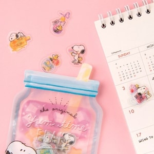 May include: A clear plastic bag with a blue zipper and a straw on top. The bag has a pink background with the text "the original Yum Time" printed on it. There are several clear stickers with cartoon characters on the bag. The stickers feature a cartoon dog with a red nose and a yellow collar.