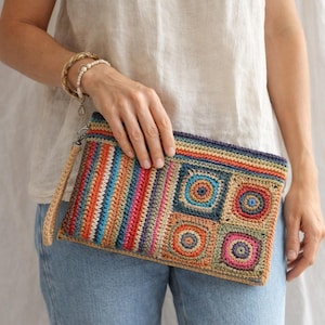 May include: A colorful, rectangular crochet clutch with a wrist strap. The clutch features a striped pattern on the left side and square and circular designs on the right. The color palette includes shades of blue, orange, pink, and green.