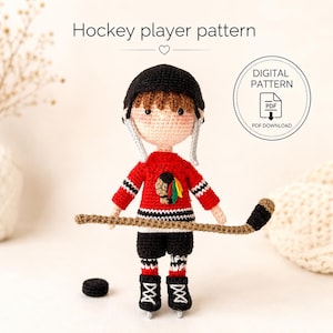 Peut inclure: Une poupée de joueur de hockey au crochet portant un casque noir, un maillot rouge avec un emblème noir et jaune, un short noir et des patins noirs. La poupée tient une crosse de hockey beige et un palet noir. Texte Hockey player pattern.