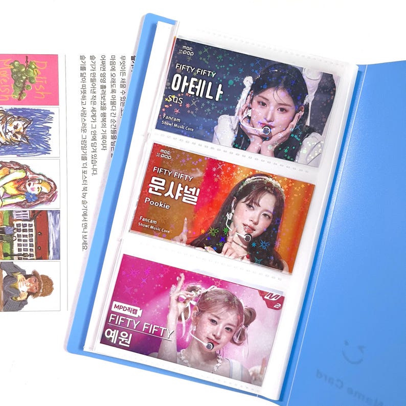 May include: A blue card holder with three photo card slots, each containing a different image of a female K-pop singer. The cards have Korean text and the group name "FIFTY FIFTY". The holder is open, revealing the cards.