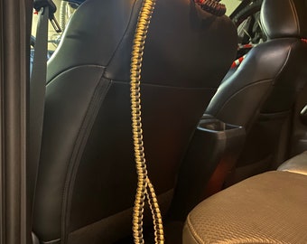 May include: A black and tan paracord strap hanging from the headrest of a black leather car seat.