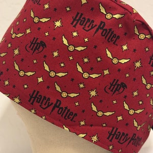 May include: Red and gold fabric scrub hat with a repeating pattern of stars, golden snitches, and the words "Harry Potter".