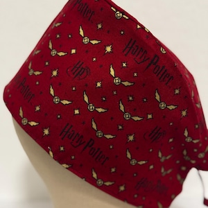 May include: Red fabric scrub hat with a repeating pattern of gold stars, flying golden snitches, and the text "Harry Potter" and "HP".
