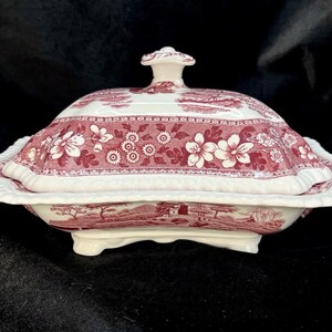May include: A white porcelain serving dish with a pink floral design and a lid. The dish has a scalloped edge and a raised center.