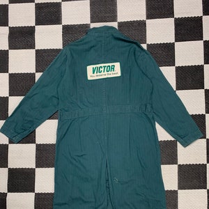 May include: A dark green workwear jacket with a white patch on the back that says "VICTOR. You deserve the best."