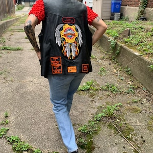 May include: Black leather vest with a large embroidered patch featuring a Native American headdress and the words "Lady Bikers". The vest also has several smaller patches, including "I'm a Vietnam Vet", "Support Big Hull "Bows", "Al Wheelers Big Al", and "Roadbert Motorcycles".