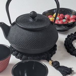 May include: Black cast iron teapot with a black woven coaster, two black teacups, and a black bowl filled with red and yellow candies.