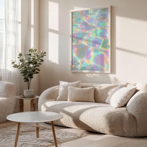 Pode incluir: Uma impress&atilde;o de arte de parede emoldurada com um design abstrato iridescente com as palavras "Blessed Aura" em branco. A obra de arte est&aacute; pendurada acima de um sof&aacute; curvo creme com almofadas a condizer. Uma mesa de centro redonda e branca e uma pequena planta em vaso tamb&eacute;m s&atilde;o vis&iacute;veis.