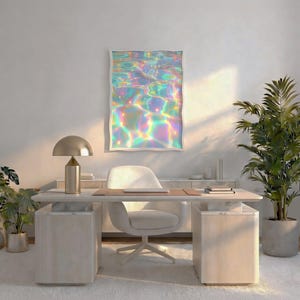 May include: A rectangular wall art print featuring a vibrant, iridescent water surface with shimmering rainbow light reflections in shades of blue, pink, and yellow, displayed in a white frame above a desk in a bright room.