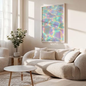 May include: A framed art print featuring an abstract, iridescent design reminiscent of water reflections. The artwork hangs above a beige, curved sofa with several pillows. A round white coffee table and a small potted plant are also visible.
