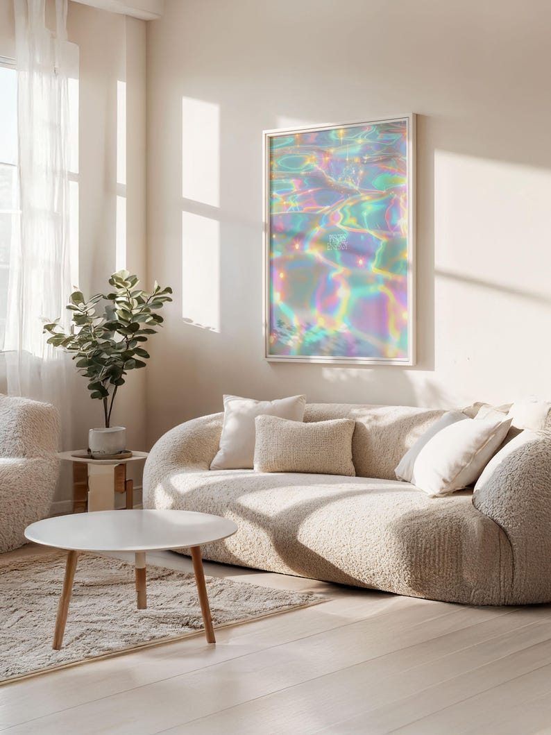 May include: A framed art print featuring an abstract, iridescent design reminiscent of water reflections. The artwork hangs above a beige, curved sofa with several pillows. A round white coffee table and a small potted plant are also visible.
