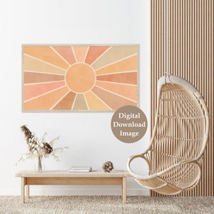 Puede incluir: Una imagen de descarga digital de un dise&ntilde;o de rayos de sol en tonos naranja, melocot&oacute;n y marr&oacute;n. El sol est&aacute; enmarcado en un marco de madera clara y est&aacute; colgado en una pared blanca. La imagen est&aacute; en un ambiente de sala de estar con una silla colgante de mimbre y una mesa de madera con un jarr&oacute;n de flores secas.