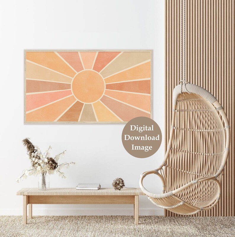 Puede incluir: Una imagen de descarga digital de un dise&ntilde;o de rayos de sol en tonos naranja, melocot&oacute;n y marr&oacute;n. El sol est&aacute; enmarcado en un marco de madera clara y est&aacute; colgado en una pared blanca. La imagen est&aacute; en un ambiente de sala de estar con una silla colgante de mimbre y una mesa de madera con un jarr&oacute;n de flores secas.