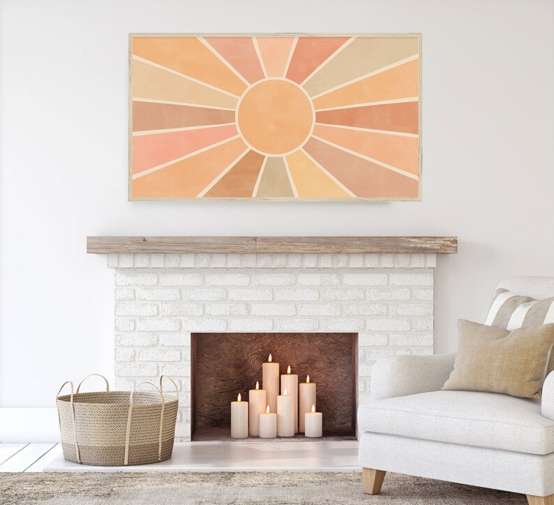 Puede incluir: Una obra de arte abstracta con forma de sol radiante, en color beige y naranja, cuelga sobre una chimenea de ladrillo blanco con velas encendidas en su interior. La obra de arte est&aacute; enmarcada en un marco de madera clara.