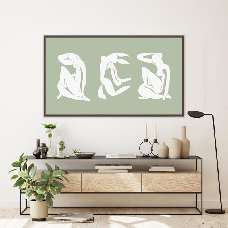 Puede incluir: Una impresi&oacute;n enmarcada con un fondo verde salvia y tres siluetas blancas de figuras en diferentes poses. Las figuras son estilizadas y abstractas.
