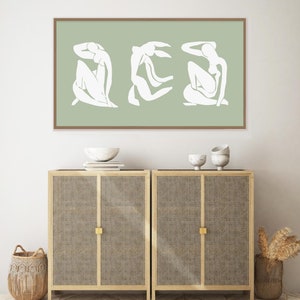 Puede incluir: Una impresi&oacute;n enmarcada con un dise&ntilde;o minimalista que presenta tres figuras blancas sobre un fondo verde salvia.