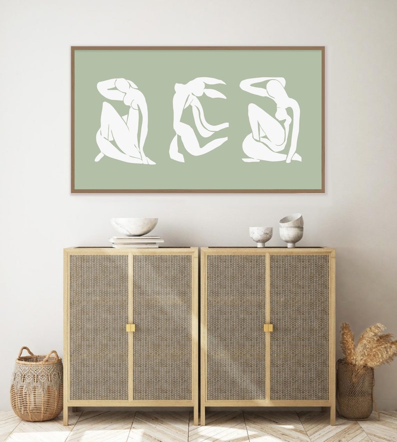 Puede incluir: Una impresi&oacute;n enmarcada con un dise&ntilde;o minimalista que presenta tres figuras blancas sobre un fondo verde salvia.