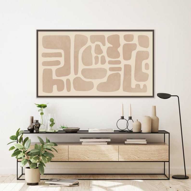 Puede incluir: Una impresi&oacute;n de arte abstracto enmarcada con un fondo beige y un patr&oacute;n de formas irregulares de color marr&oacute;n claro. La impresi&oacute;n est&aacute; colgada en una pared blanca sobre una mesa consola de madera con un marco de metal negro. La mesa est&aacute; decorada con plantas, jarrones y velas.