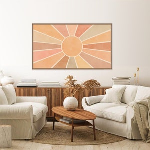 Puede incluir: Un dise&ntilde;o de interior de sala de estar con dos sof&aacute;s blancos, una mesa de caf&eacute; de madera y una impresi&oacute;n enmarcada de un dise&ntilde;o de sol en forma de rayos en tonos naranja, melocot&oacute;n y beige. La impresi&oacute;n est&aacute; colgada en una pared blanca sobre un gabinete de madera.