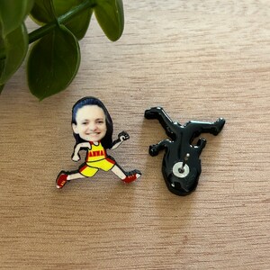 May include: A pair of stud earrings featuring a cartoon-style runner with a photographic face. The runner wears a yellow and red tank top with the name ANNA printed in red. The back of the earring shows a black silhouette with a metal post and clutch.