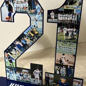 Puede incluir: Un n&uacute;mero 21 azul y blanco hecho de acr&iacute;lico con fotos de un jugador de f&uacute;tbol y un equipo. La base del n&uacute;mero es azul con letras blancas que dicen "HUNTER SHAY #21".
