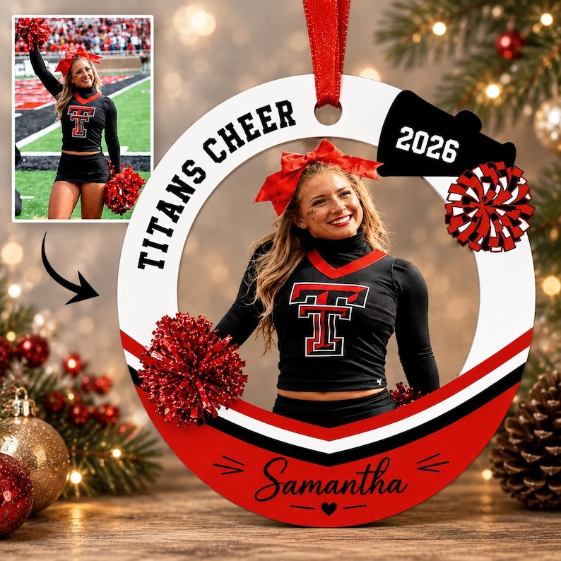 K&ouml;nnte beinhalten: Ein kreisf&ouml;rmiger wei&szlig;-roter Weihnachtsschmuck mit einem Foto einer Cheerleaderin in schwarzer Uniform mit rotem T-Logo. Das Ornament enth&auml;lt den Text TITANS CHEER, das Jahr 2026, eine rote Schleife, einen roten Pompon und den Namen Samantha.