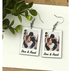 May include: A pair of white wooden earrings with a photo of a couple and the text "Steve & Hannah" on each earring.