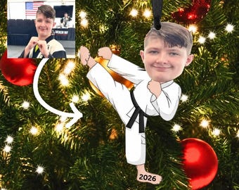 May include: A custom Christmas ornament featuring a cartoon illustration of a person in a white karate uniform with a black belt, performing a high kick. The figure has a realistic photo of a face attached, and the year 2026 is printed on one foot.