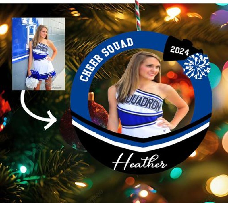 K&ouml;nnte beinhalten: Ein runder Weihnachtsschmuck mit blau-schwarzem Rand, der den Text CHEER SQUAD, 2024 und den Namen Heather tr&auml;gt. In der Mitte befindet sich ein Foto einer Person in einer blau-wei&szlig;en Cheerleader-Uniform, die einen blauen Pompon h&auml;lt.