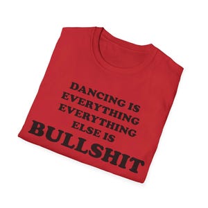 May include: A bright red short-sleeved t-shirt featuring bold black text printed on the front. The text reads: DANCING IS EVERYTHING EVERYTHING EVERYTHING ELSE IS BULLSHIT. The shirt has a classic crew neckline and is folded neatly.
