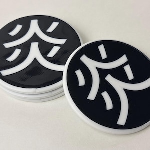 May include: A set of black and white coasters featuring a Japanese symbol. The coasters are circular with a white edge and a black centre displaying a white abstract design. They are stacked on a white surface.