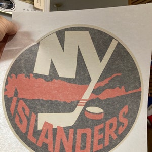 May include: A black and white circular logo with the text "NY ISLANDERS" in red. The logo features a hockey stick and a puck.