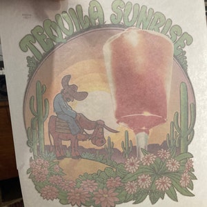 May include: A vintage print featuring a Tequila Sunrise cocktail illustration. The design includes a cowboy riding a donkey in a desert landscape with cacti and flowers. The cocktail glass is large and prominent.