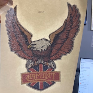May include: A vintage iron-on patch featuring a brown eagle with a white head and a red, white, and blue Union Jack shield with the word "Triumph" in gold lettering.