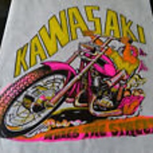 May include: White t-shirt featuring a colorful graphic of a motorcycle with the word "KAWASAKI" above it. The motorcycle is pink, orange, and black. The text "Raked and Chopped" is below the motorcycle.