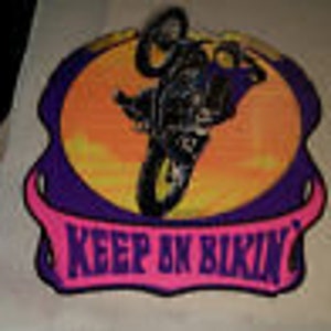 May include: A colorful iron-on patch featuring a cartoon illustration of a person riding a motorcycle with the words "Keep on Biking" in a banner below.