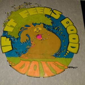 May include: A yellow, green, and blue circular design with the text "It Feels Good Doin'" and a cartoon bear with a pink tongue sticking out. The design is on a white background.