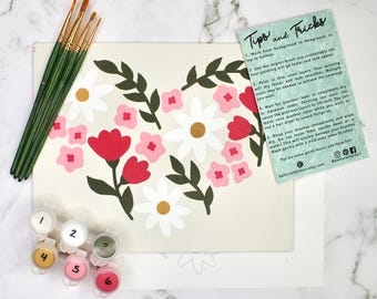 May include: A paint-by-numbers kit featuring a floral design with red, pink, and white flowers, green leaves, and paint pots. The kit includes paintbrushes and a card with tips and tricks for painting. The background is a light beige color.