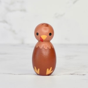 May include: A brown wooden turkey figurine with painted details. The turkey has a red wattle, yellow feet, and black eyes.
