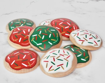 Può includere: Un set di nove biscotti di legno decorati con glassa rossa, verde e bianca e codette colorate.