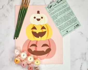 May include: A paint-by-numbers kit with a stacked pumpkin design. The kit includes paint pots, paintbrushes, and a card with painting tips. The pumpkins are in shades of pink, yellow, and white. The card reads "Tips and Tricks".