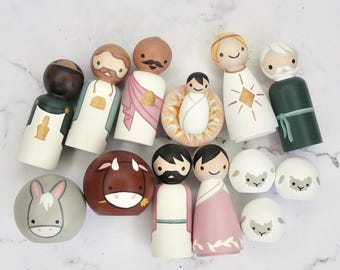 May include: A set of wooden figurines depicting the Nativity scene. The figures include Mary, Joseph, baby Jesus, the three wise men, a donkey, a cow, and two sheep. The figures are painted in bright colors and have simple, childlike features.