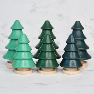 May include: Set of six wooden toy trees in three different shades of green. The trees are stacked in tiers and have a smooth, painted finish.