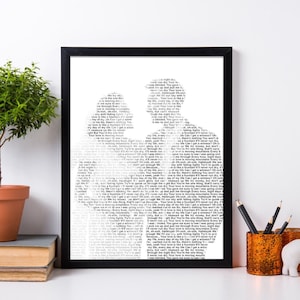 Op de afbeelding: Een zwart ingelijst afdruk van een stel dat in wit is gesilhouetteerd. De silhouet is gemaakt van tekst, die te klein is om te lezen. De afdruk staat op een witte plank met een plant in een pot, een stapel boeken en een potloodhouder.